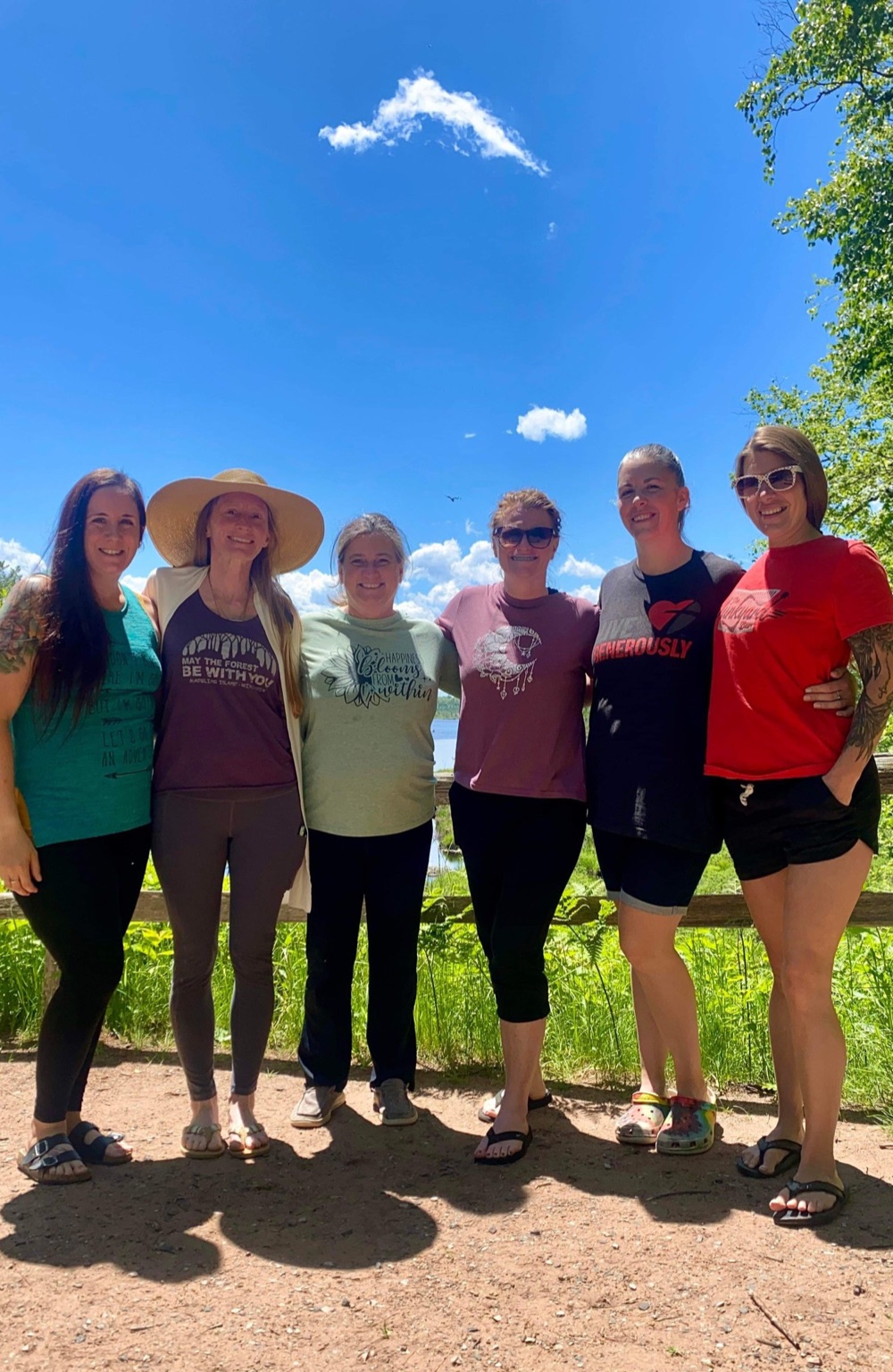 Six women standing arm in arm in the sun by the lake