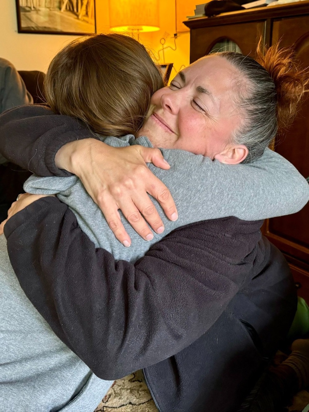 Two retreat participants in a long hug indoors, one smiling with her eyes closed